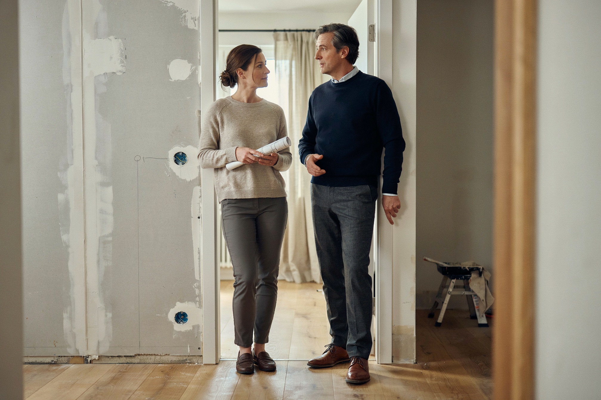 Zwei Personen mit Plänen vor einer aufgerissenen Wand in der Wohnung